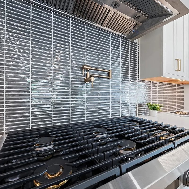 Pewter stacked tile running behind a range, under a steel hood.