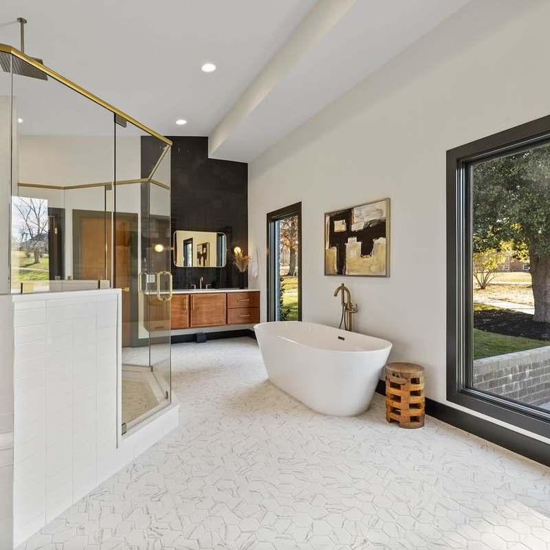 Freestanding tub against a wall of pale stone tile, with unlacquered brass fittings.