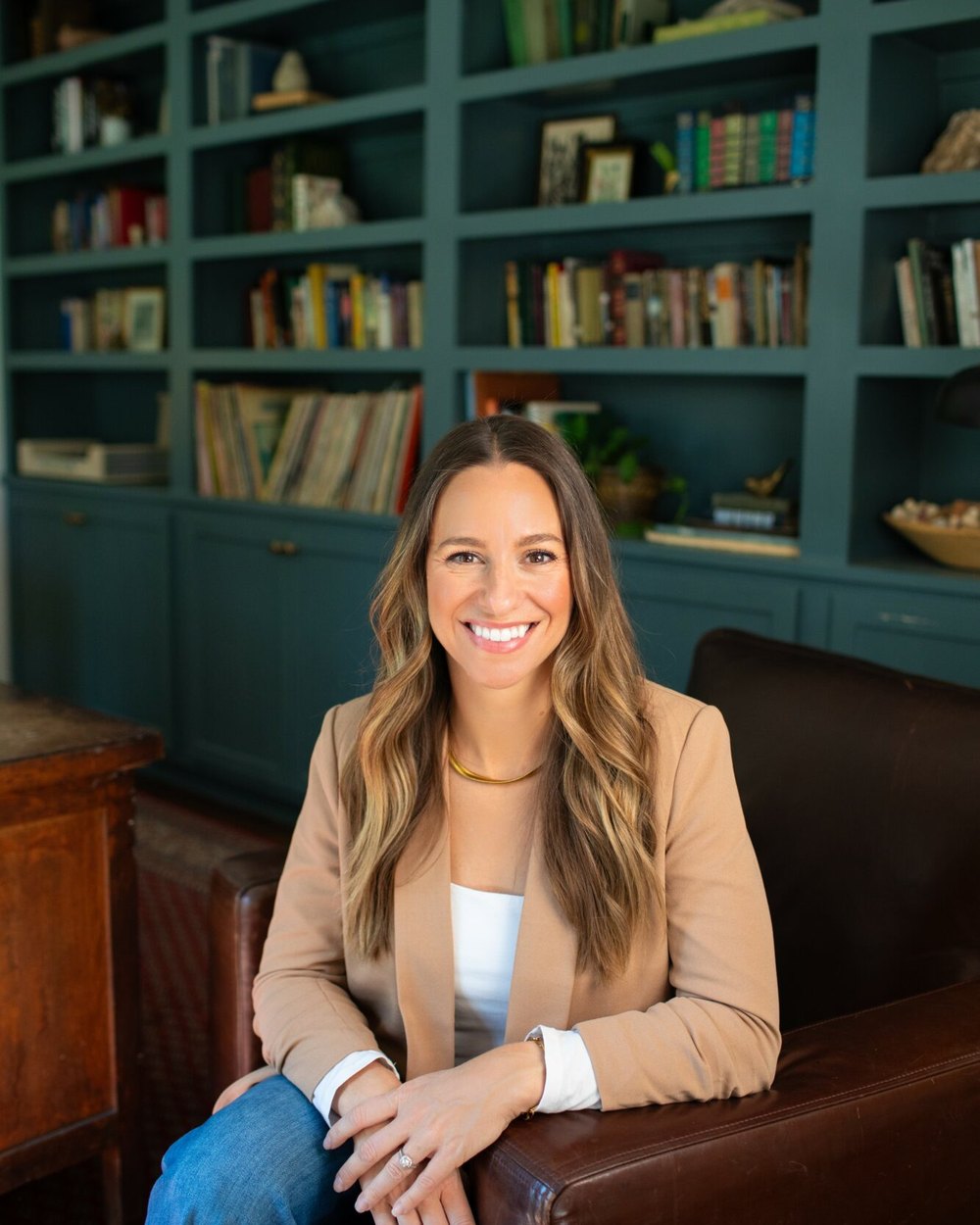 Natalie Mayes seated in front of a wall of deep teal built in bookshelves.