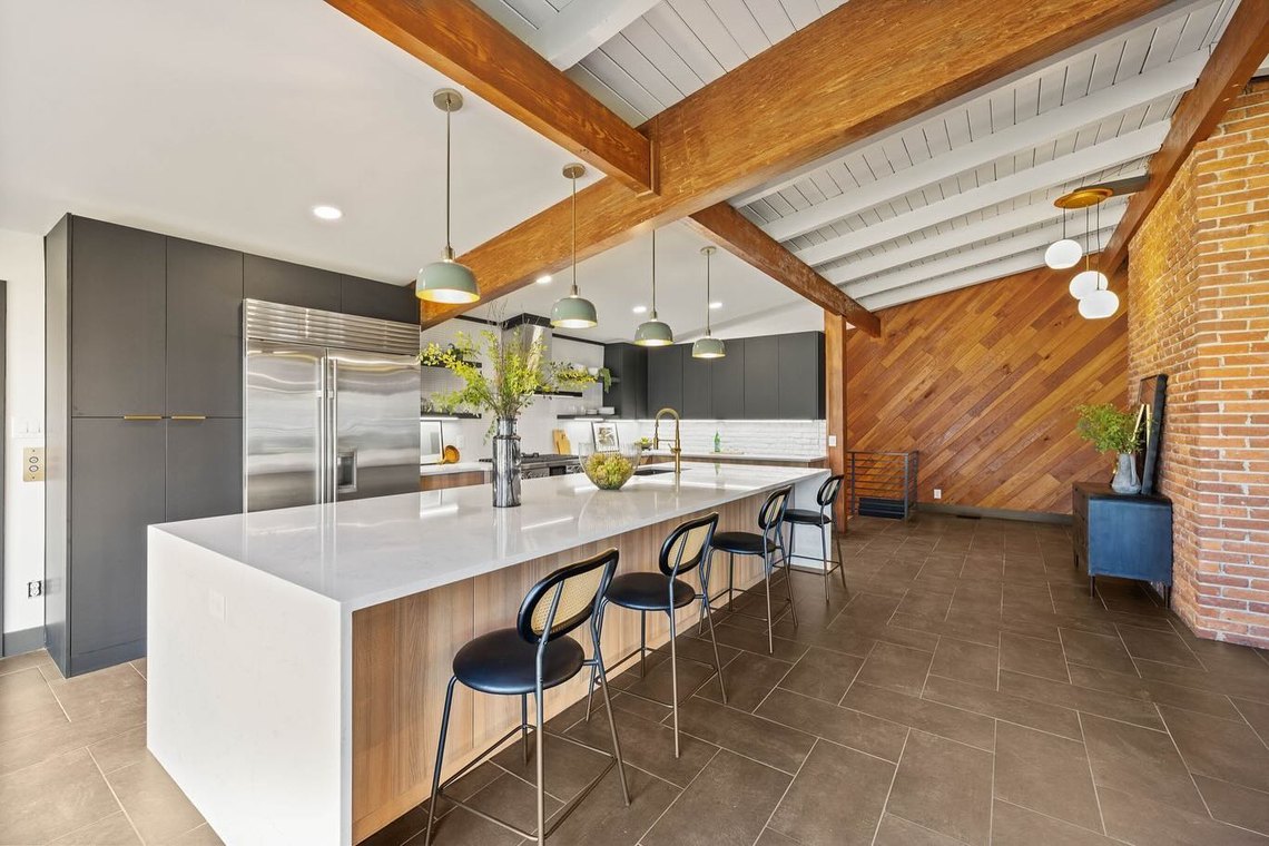 Kitchen under a vaulted white plank ceiling with stained timber beams and a long island.