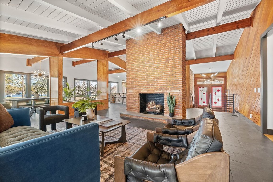 Living room with a full height brick fireplace, timber beams and a vaulted plank ceiling.