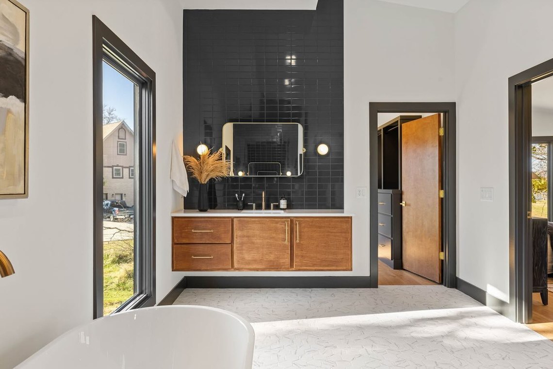 Bathroom in dark stacked tile with a floating oak vanity and a black framed window.