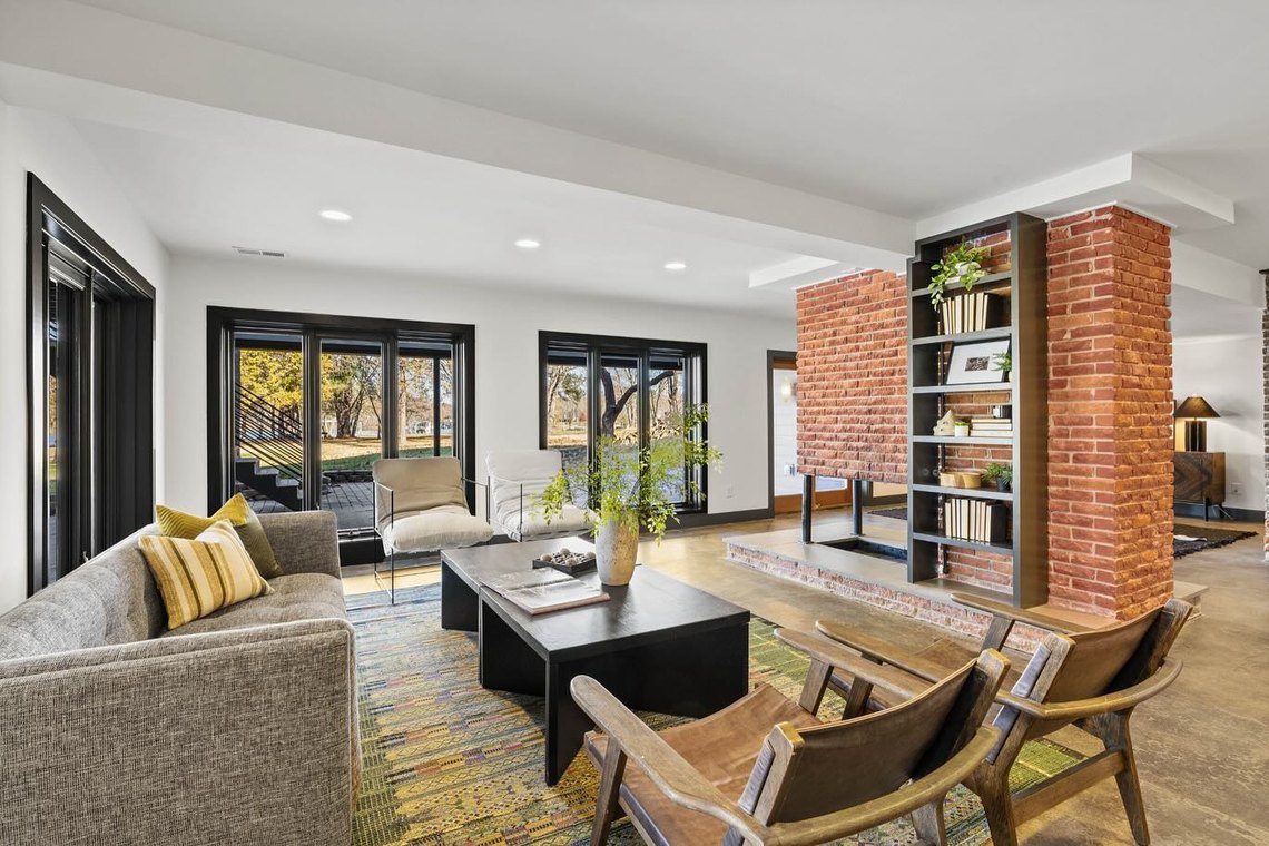 Living room with a brick wall, black steel windows and mid century seating on a patterned rug.