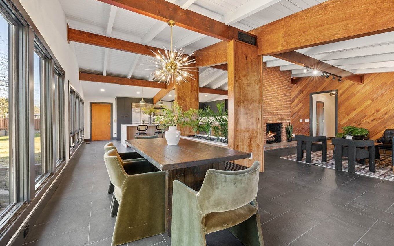 Dining room under exposed walnut beams, with a brick chimney breast and a brass starburst chandelier.