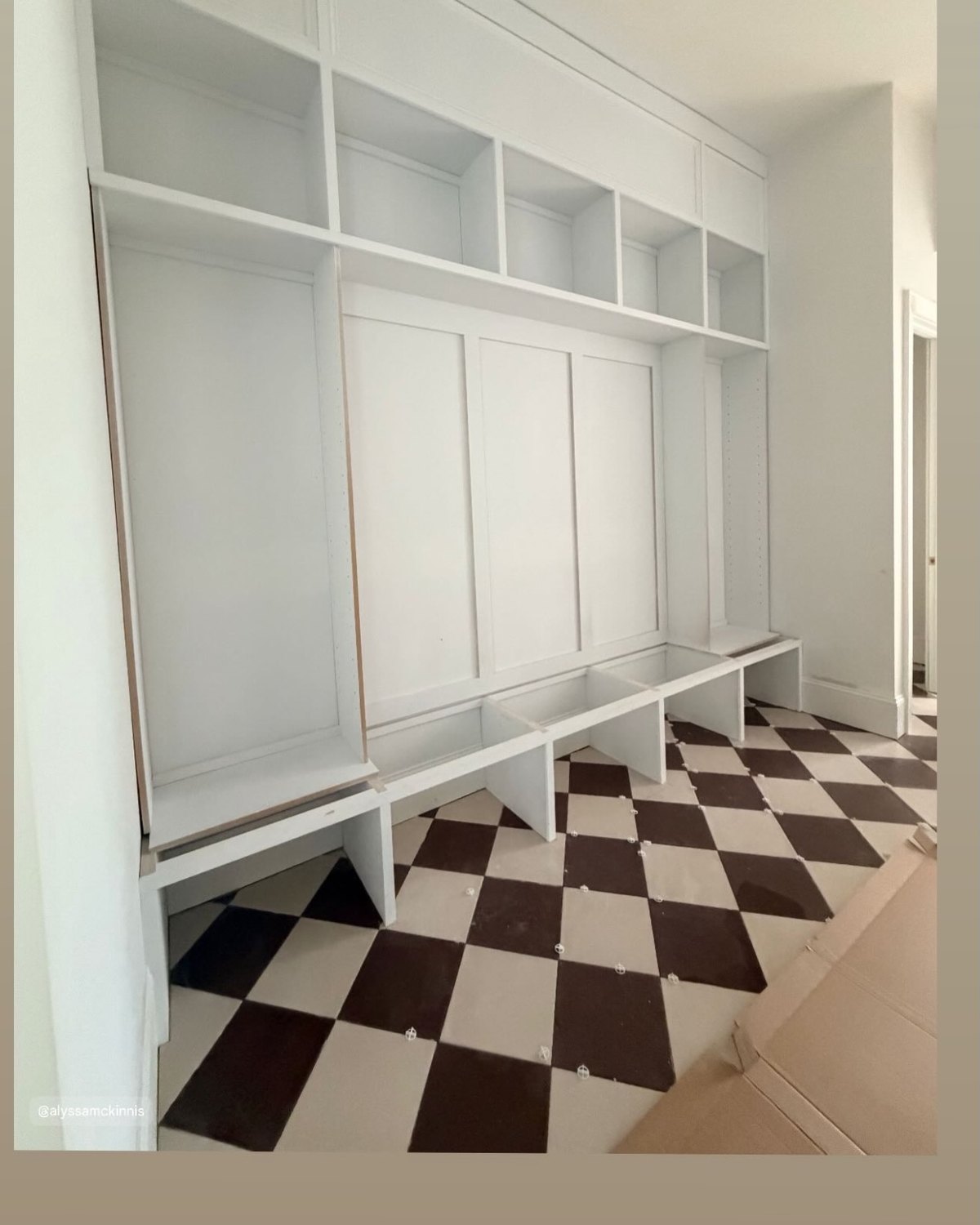 The same checkerboard floor installed, running under a wall of white built in lockers and a bench.